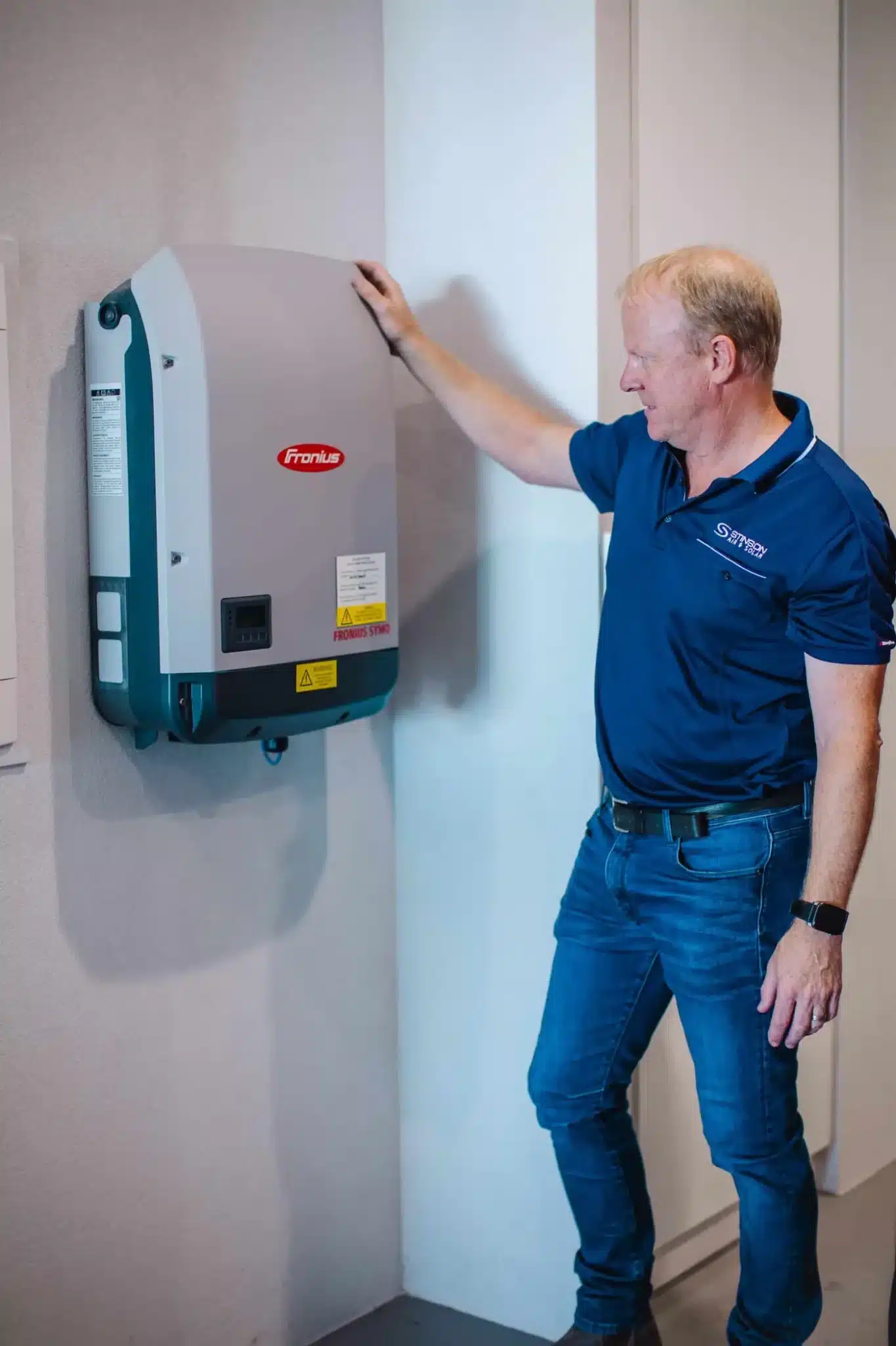 Technician inspecting wall-mounted Fronius solar inverter in residential setting